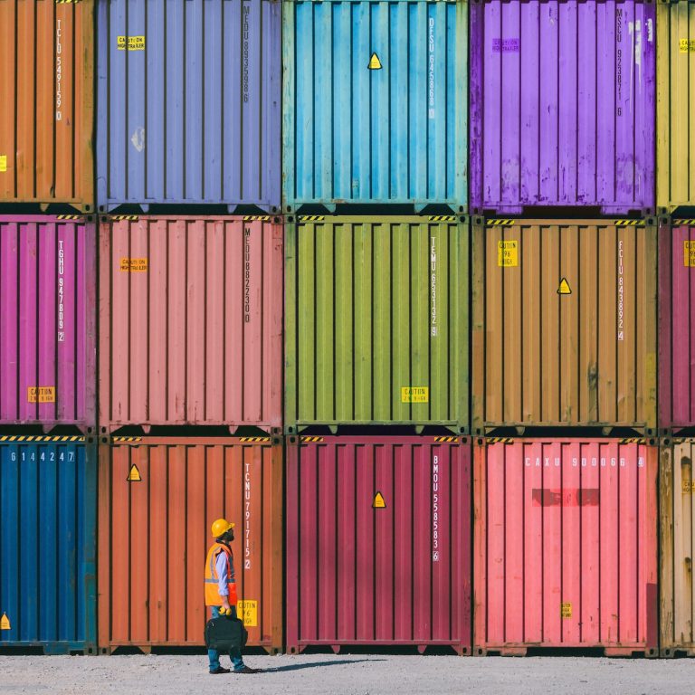 Engineer man with yellow crash helmet and worker west checking cargo freights in front of colorful cargo container stacks in shipping port
