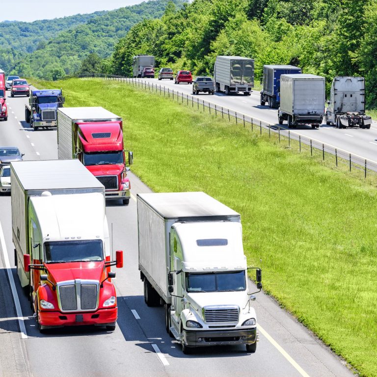 A heavy flow of 18-wheelers peppered with cars and SUVs roll down a Tennessee interstate highway.  Heat rising from the pavement gives a shimmering effect to vehicles and background in the distance.